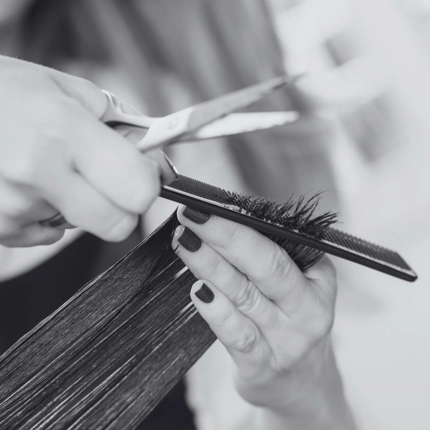 Mãos cortando uma mecha de cabelo com tesoura e pente