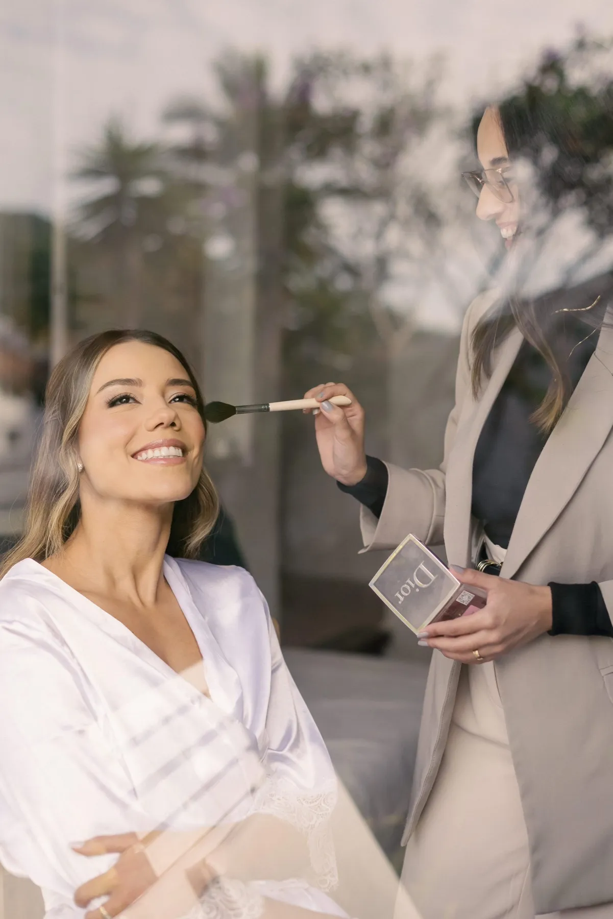 Noiva sorrindo enquanto a maquiadora finaliza a pele